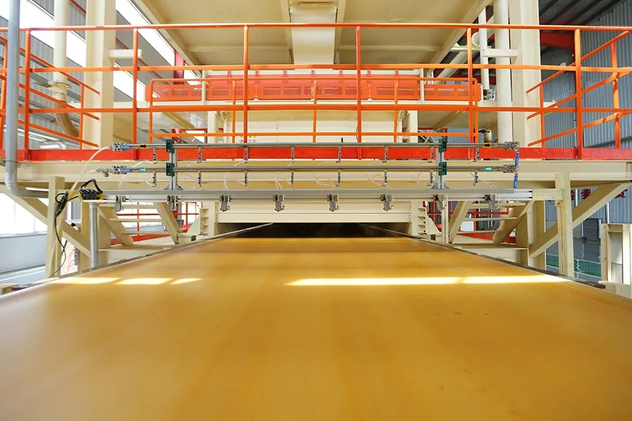 Board exiting a Ningfeng continuous press, low angle down the conveyor, the panel surface glowing