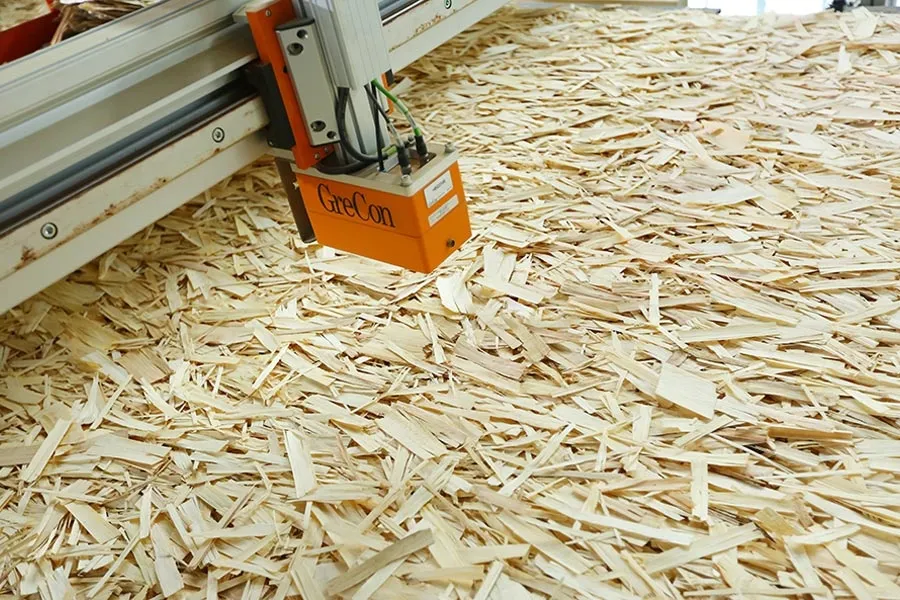 GreCon quality sensor suspended over a loose wood-strand mat on a Ningfeng production line